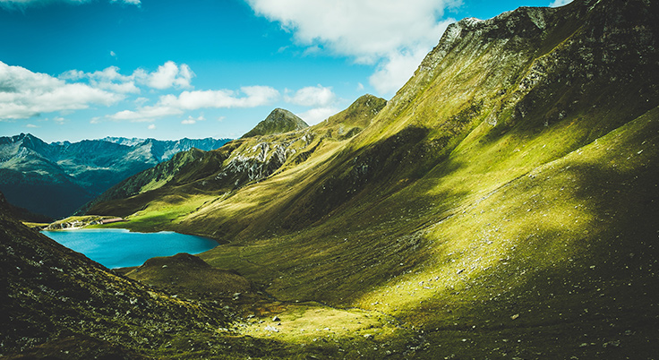 Paisaje montañoso con un prado y lago al fondo